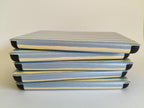 One More Chapter Premium Kindle Case in Rainy Sunday – five cases stacked flat, side-on view showing dusty blue and cream stripe spine texture