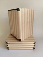 One More Chapter Premium Kindle Case in Barista Blend – open folio propped on stack of closed cases, warm cream and taupe stripe
