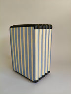 One More Chapter Premium Kindle Case in Rainy Sunday – five dusty blue and cream stripe folios fanned upright, spine-side view with black corner detail