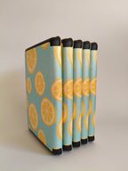 One More Chapter Premium Kindle Case in Lemon Grove – five sky blue lemon slice print folios fanned upright, spine-side view
