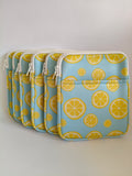 One More Chapter E-reader Sleeve in Lemon Grove – four sky blue sleeves with yellow lemon slice print lined up, angled front view showing zip and front pocket