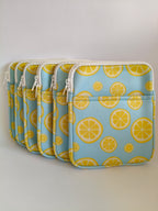One More Chapter E-reader Sleeve in Lemon Grove – four sky blue sleeves with yellow lemon slice print lined up, angled front view showing zip and front pocket