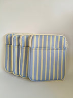 One More Chapter E-reader Sleeve in Rainy Sunday – four periwinkle blue and cream stripe padded sleeves lined up, angled front view showing zip and front pocket