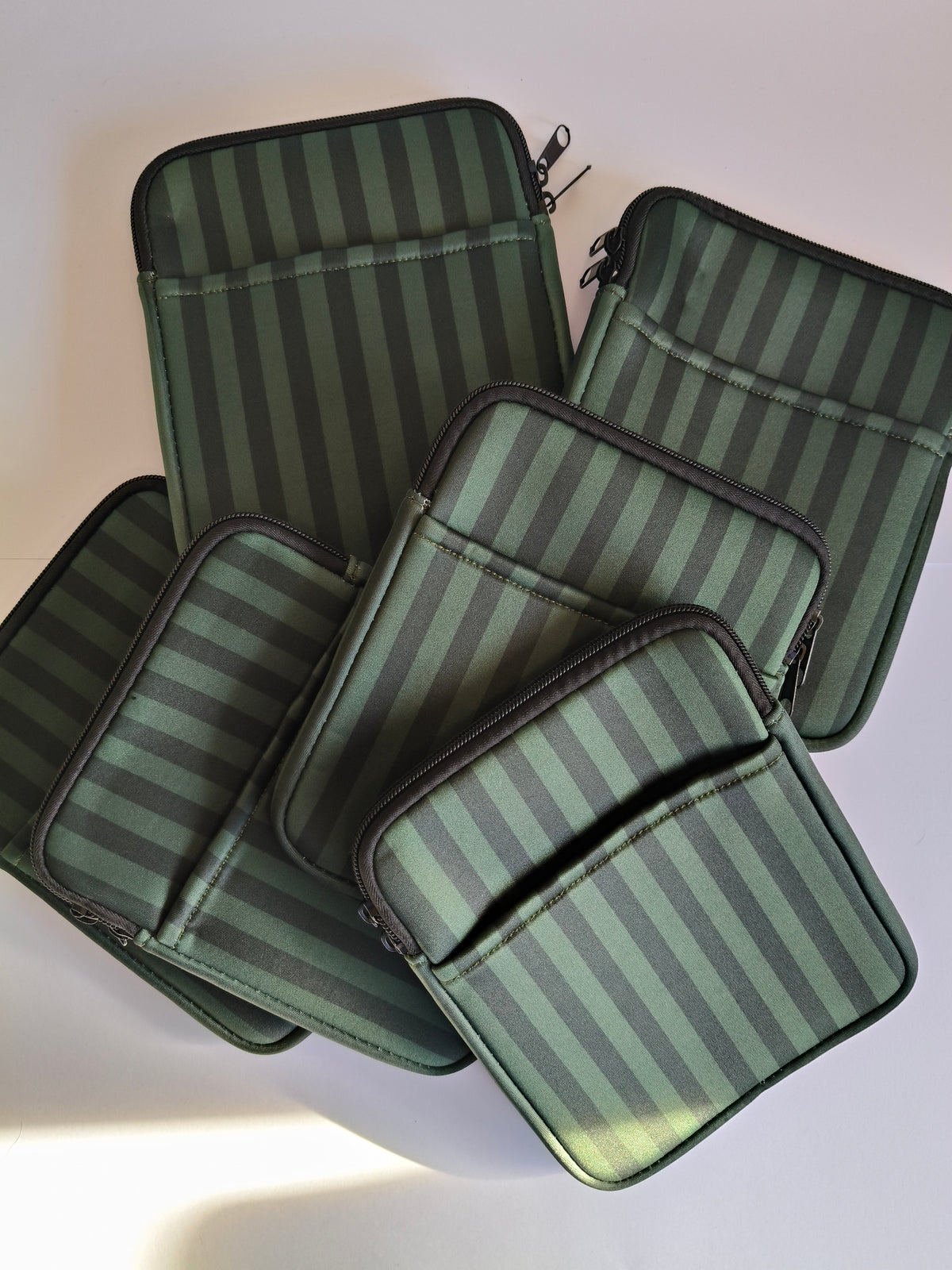 One More Chapter E-reader Sleeve in Midnight Library – five deep forest green tonal stripe sleeves scattered, top-down flat lay